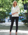 A model stands outdoors wearing black treggings and a white top, complemented by heels and a handbag.