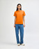 A heavyweight unisex t-shirt in bright orange, paired with light blue baggy jeans, modeled by a young person.