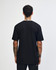 A person wearing a black unisex short sleeve t-shirt, viewed from the back, with a slight curl in the hair.