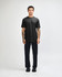 A black unisex short sleeve t-shirt worn with light blue baggy jeans and black sneakers. The model poses against a plain background.