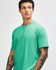 A model wearing a unisex short sleeve T-shirt in vibrant mint green, featuring a logo on the sleeve.