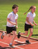 Two children running on a track, wearing white T-shirts and black shorts.