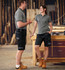 Unisex utility stretch cargo work shorts in black, paired with grey tops, alongside two models in a workshop setting.