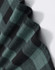 A close-up of a unisex flannel shirt in black and green plaid fabric, featuring a logo.