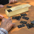 A wooden box containing black dominoes scattered on a table, with hands visible playing the game.