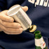 A drink bottle opener in silver, featuring a rounded design and a branding logo, being used to open a green bottle.
