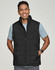 A man wearing a black insulated puffer vest with a 3D cut over a grey shirt, smiling. The vest has a logo.
