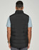 A black insulated puffer vest with a 3D cut, viewed from the back, worn over a light blue shirt.