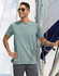 Men's premium cotton short sleeve T-shirt in a soft green shade, featuring a logo, worn by a man on a sailboat.