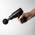 A black massage gun with a spherical attachment held in a hand, featuring a sleek design and a logo.