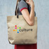 A beige tote bag with a logo and colourful dots, held by a person wearing a striped top.