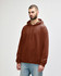 A brown hooded sweatshirt with a front pocket and drawstrings, worn by a model in casual attire.