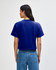 A blue boxy t-shirt with short sleeves and a back view. The model wears high-waisted jeans and has curly hair.