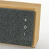 A bamboo Bluetooth speaker with a grey fabric front, featuring control buttons and a logo.
