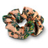 A peach patterned hair scrunchie with green floral designs, featuring a subtle sheen and a soft fabric texture.