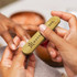 A bamboo nail file in a natural bamboo finish, held between two hands during a manicure session.