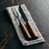 A cheese carving set featuring a knife and fork with wooden handles, positioned on a linen cloth.