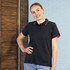 A black women's polo shirt with red collar and sleeves, featuring a logo, displayed against a brick wall background.