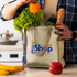 A beige tote bag filled with lettuce, broccoli, a bell pepper, an eggplant, and a baguette, featuring a logo.