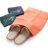 An orange drawstring pouch with slippers peeking out, accompanied by two flat bags in navy and green.