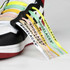 Colourful printed shoelaces in white, pink, yellow, green, and black attached to a sneaker with a logo.