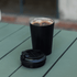 A double-walled black coffee cup with a lid, positioned on a green table.