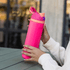 A drink bottle in vibrant pink with a matching cap and a handle, featuring a logo on one side.