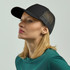 A black trucker cap with a mesh back, displayed on a model with blonde hair.