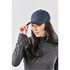 A woman adjusts a navy blue cap while wearing a grey long-sleeve top. The cap features a logo.