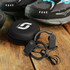 Runner Bluetooth earbuds in black, with a compact carrying case, displayed on a wooden surface beside sports shoes.