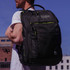 A black backpack with green accents, featuring a logo and multiple compartments, worn by a person.