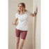 A woman in a white t-shirt and burgundy shorts leans against a wall, highlighting the activewear style.