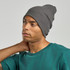 A grey beanie made from recycled polyester, worn by a model with a green top. The beanie has a ribbed texture and a logo.