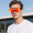 Frameless sports sunglasses with a vibrant red-orange tint worn by a male model against a blue sky backdrop.