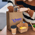 A large flat handle paper bag in brown with a logo, accompanied by a takeaway container and a coffee cup.
