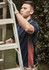 A man in a navy blue short sleeve polo with an orange and white design on the side, climbing a ladder outdoors.