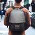 A grey and charcoal backpack with a logo, worn by a person standing on a city street.