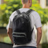 A black foldable backpack with green accents is worn by a person, set against a blurred outdoor background.