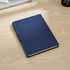 A navy blue hardcover notebook with a textured cover, resting on a wooden desk. It features a logo on the front.