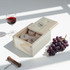 A wooden box containing wine stoppers, with a glass of red wine and a bunch of purple grapes beside it.