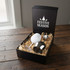 A gift box containing a white egg and a stainless steel wine glass, resting on straw. The box has a festive design.