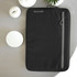 A black laptop sleeve featuring a front zipper pocket and a logo. Set against a neutral background with candles.