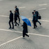 A group of people walking on a pavement, with one person holding a blue umbrella.