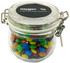A glass canister filled with colourful mini M&Ms, featuring a metal clasp and a logo on the lid.