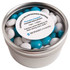 A small round tin filled with chewy fruit sweets in turquoise, white, and grey. The tin has a label on top.
