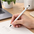 A sleek white aluminium inkless pen rests in a hand above a notepad with handwritten notes and a laptop in the background.