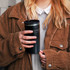 A travel mug with a double wall, featuring a black exterior and a lid, held by a person in a corduroy jacket.