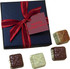 A dark blue gift box tied with a red ribbon containing four different chocolates in various colours.