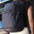 A black backpack with multiple compartments and adjustable straps, worn by a person from behind.