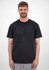 A man stands wearing a plain black short sleeve tee, with a neutral background. The tee features a logo.